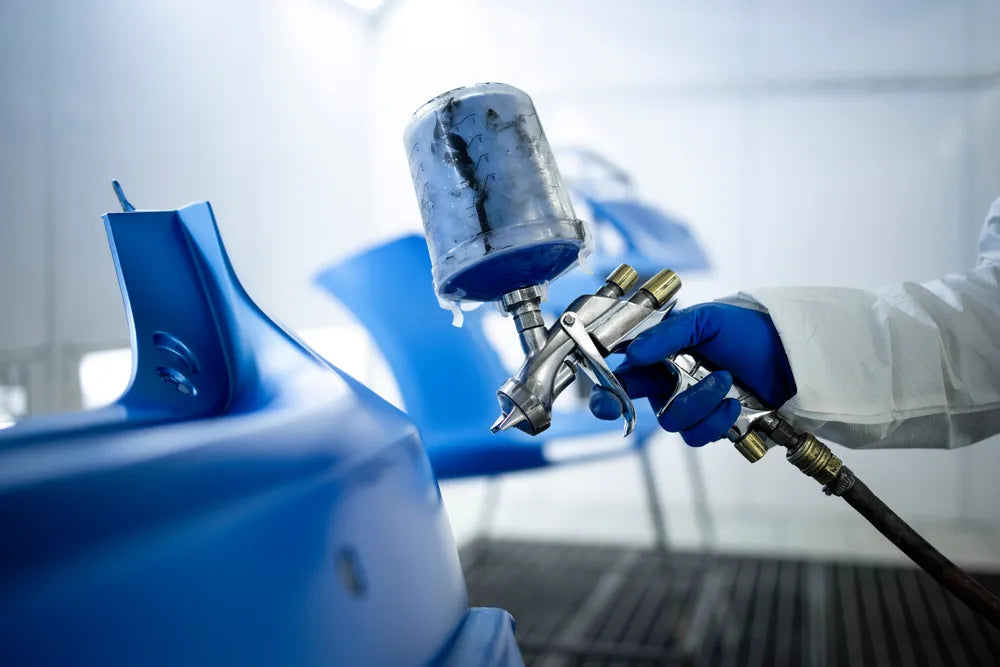 Hand holding an automotive aerosol spray can, applying paint evenly to a car surface
