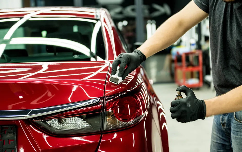 Hand using a microfiber cloth to remove aerosol spray paint from a car without damaging the surface