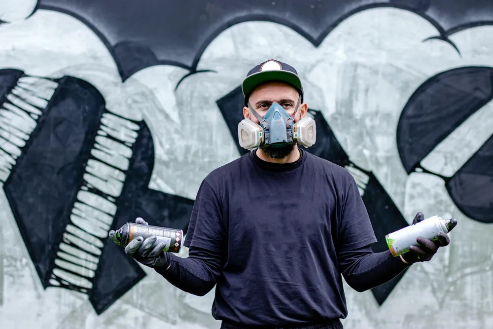 Person wearing an aerosol mask while spray painting a wall with an aerosol can 