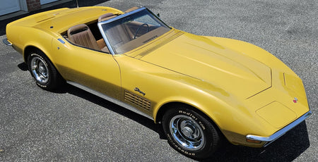 A yellow classic Corvette convertible sports car parked outdoors on a gray asphalt surface.